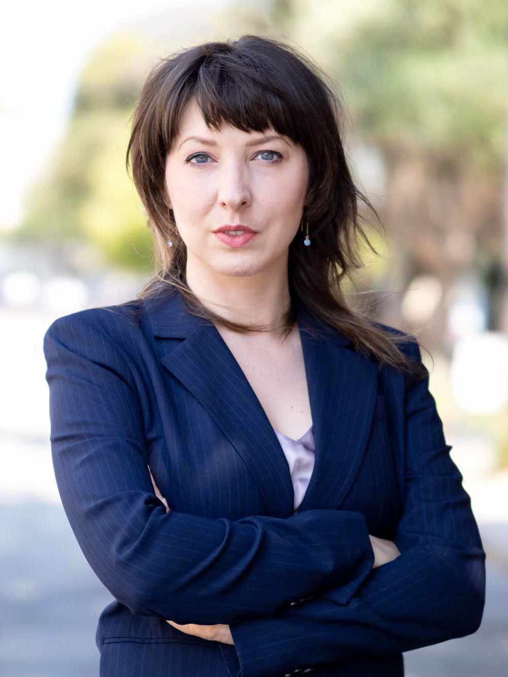 A portrait photograph of Genevieve K. Guertin wearing a suit and standing confidently in a San Francisco street. 
